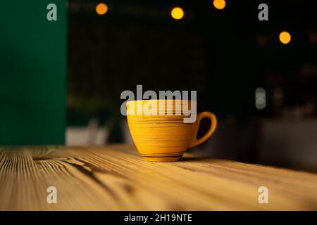 Leuchtend orange Tasse auf einem unscharfen dunklen Hintergrund mit Bokeh. Stockfoto