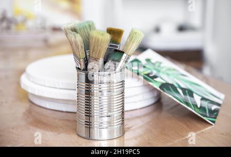 Die Metallkistchen mit den Pinsel der Farbe und die Leinwand mit dem Bild der Monstera. Stockfoto