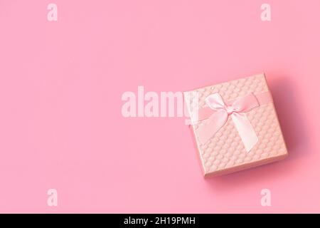 Draufsicht auf rosa Geschenkbox mit Satinschleife auf pastellrosa Hintergrund mit Copy Space. Flat Lay Komposition für Hochzeit, Geburtstag, Glücklichen Frauentag, Muttertag, Valentinstag. Stockfoto