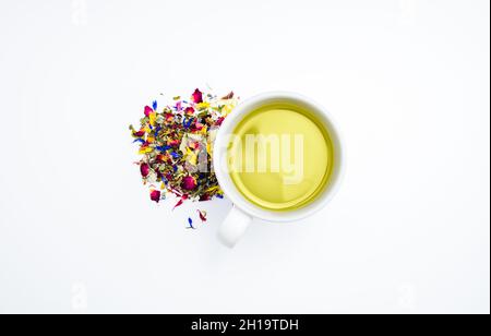 Getrockneter Kräutertee hinterlässt neben einer Tasse heißen, frisch gebrühten Tees auf weißem Hintergrund. Stockfoto