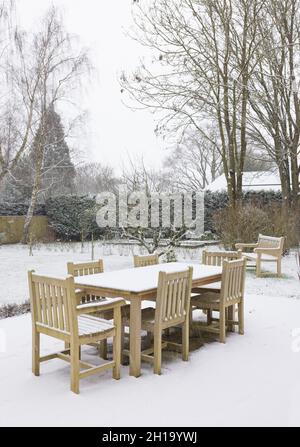 Schnee fällt auf Gartenmöbeln im Winter, Großbritannien. Tisch und Stühle aus Teakholz-Hartholz in einem großen Hinterhof Stockfoto