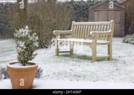 Hinterhof (Hinterhof) im Winter mit Schnee bedeckt, mit einer Teakholz-Holzbank auf dem Rasen. England, Großbritannien Stockfoto