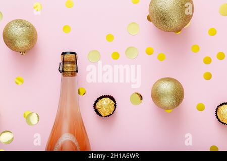 Rosa Champagner-Flasche mit Korkdeckel Konfetti und Weihnachtskugeln goldene weihnachtsdekorationen auf rosa Hintergrund. Flach liegend Nahaufnahme Stockfoto