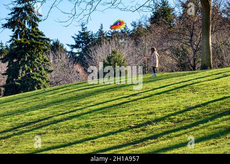 Ein junges Mädchen fliegt einen bunten Drachen an einem Wintertag, Charleson Park, Vancouver, British Columbia, Kanada. Stockfoto