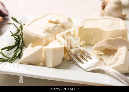 Teller mit zerdrücktem Feta-Käse auf hellem Holzhintergrund Stockfoto