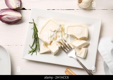 Teller mit zerdrücktem Feta-Käse auf hellem Holzhintergrund Stockfoto