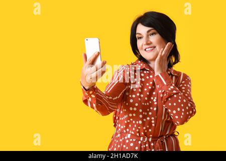 Reife Frau mit Handy, die Selfie auf gelbem Hintergrund nimmt Stockfoto