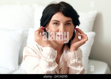 Reife Frau mit rosa Ohrstöpseln im Schlafzimmer Stockfoto