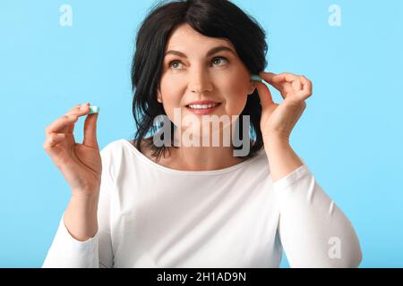 Ältere Frau, die Ohrstöpsel auf blauen Hintergrund setzt Stockfoto