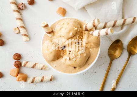 Schüssel mit leckerem Karamell-Eis mit Nüssen auf weißem Hintergrund Stockfoto