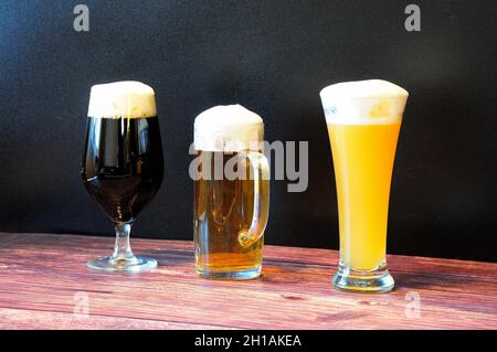 Drei verschiedene Gläser mit drei verschiedenen Bieren stehen auf einem braunen Holztisch. Nahaufnahme. Stockfoto