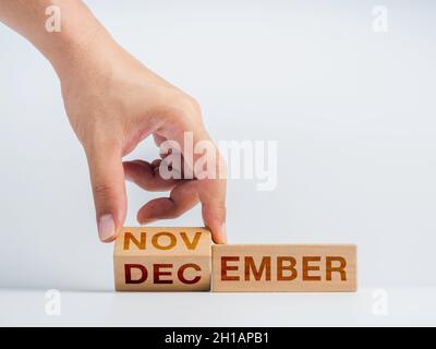 Wechsel zum letzten Monat des Jahres. Die Hand dreht Holzwürfelblöcke für Wortwechsel, Monate von November bis Dezember auf dem Schreibtisch Stockfoto