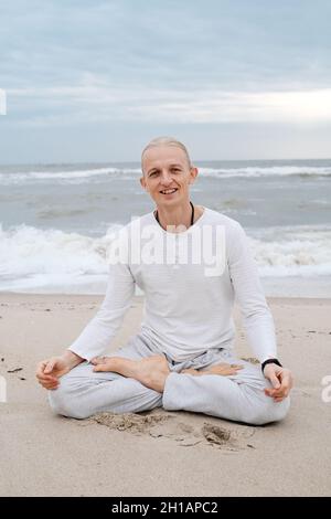 Mann macht Yoga am Strand im Herbst über Wellen im Meer. Cremig, leichter Sand und Himmel, Asanas und Meditation, Gleichgewicht im Leben, Selbstbewusstsein und Stockfoto