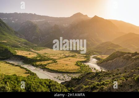 Herrlicher Sonnenuntergang über dem grünen Flusstal, umgeben von felsigen Bergen Stockfoto