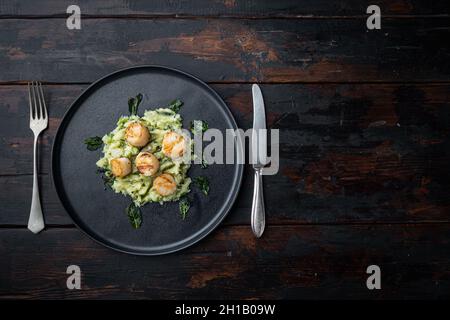 Gekochte Jakobsmuscheln mit matschierten Minzkartoffeln und grüner Erbse, flach liegend, auf dunklem Holzhintergrund mit Platz für Text Stockfoto