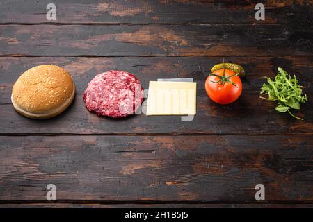 Zutaten zum Kochen von Burgern. Hacksteak-Hacksteaks, Brötchen, Tomaten, Kräuter und Gewürze, auf altem dunklen Holztisch-Hintergrund, mit Kopierplatz für t Stockfoto