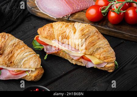 Klassisches BLT-Croissant-Sandwich-Set mit Kräutern und Zutaten auf schwarzem Holztisch Stockfoto