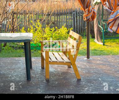 Holzbank und grüner Kunststoff-Tisch auf der Veranda in einem Landhaus, Frühjahr, im Freien. Stockfoto