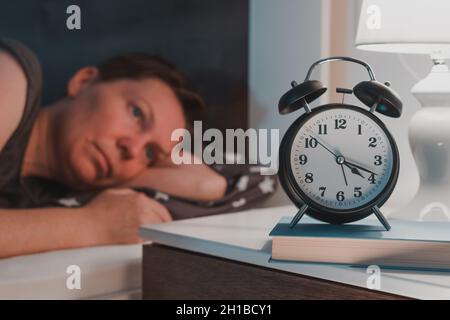 Schlaflose, insomniakale Frau, die im Bett liegt und den Wecker auf dem Nachttisch anschaut, selektiver Fokus Stockfoto