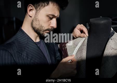 Professioneller Schneider, der Messungen für die Erstellung eines maßgeschneiderten, hochwertigen Anzugs in einem Schneideratelist anfertigte. Konzept der Mode, handgemacht, Hand cra Stockfoto