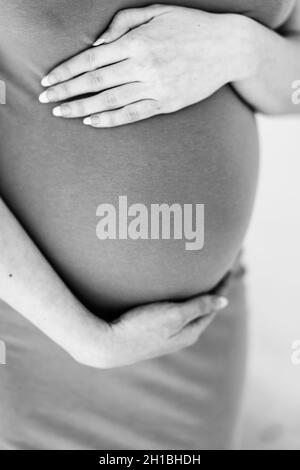 Vertikale Graustufenaufnahme einer Schwangeren, die ihren Bauch hält Stockfoto