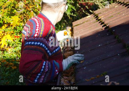 Mann, der das Dach von heruntergefallenen Blättern reinigt. Eine saubere Rinne in der Herbstsaison. Das Haus draußen halten. Hauswartung. Stockfoto