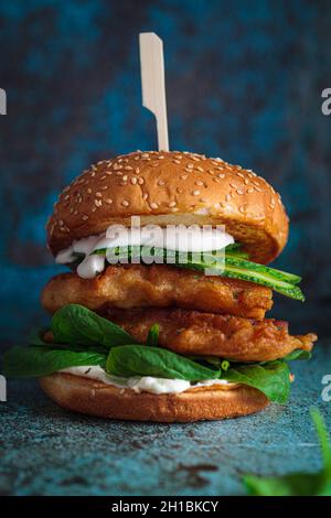 Fisch-Burger auf grauem Teller, dunkelblauer Hintergrund. Kabeljau im Teig mit Mayonnaise und Spinat-Sandwich. Stockfoto