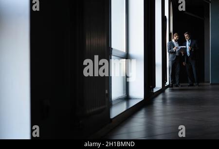 Zwei Kollegen kommunizieren auf dem Flur, Partner gehen im modernen Büro Stockfoto
