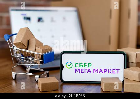 SberMegaMarket ist ein russischer Marktplatz im Besitz der Sberbank. Smartphone mit SberMegaMarket-Logo auf dem Bildschirm, dem Einkaufswagen und dem Laptop. Stockfoto