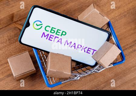 SberMegaMarket ist ein russischer Marktplatz im Besitz der Sberbank. Smartphone mit SberMegaMarket-Logo auf dem Bildschirm und Paketen im Warenkorb. Stockfoto