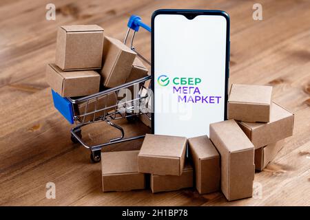 SberMegaMarket ist ein russischer Marktplatz im Besitz der Sberbank. Smartphone mit SberMegaMarket-Logo auf dem Bildschirm, Warenkorb und Paketen. Stockfoto