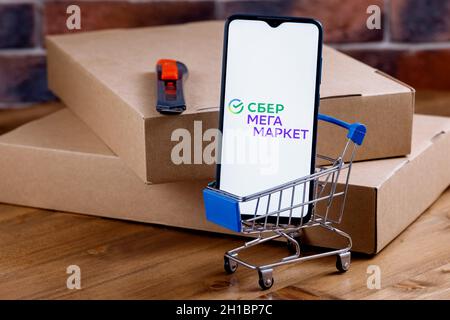 SberMegaMarket ist ein russischer Marktplatz im Besitz der Sberbank. Smartphone mit SberMegaMarket-Logo auf dem Bildschirm, Warenkorb und Paketen. Stockfoto