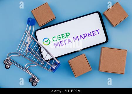 SberMegaMarket ist ein russischer Marktplatz im Besitz der Sberbank. Smartphone mit SberMegaMarket-Logo auf dem Bildschirm, Warenkorb und Paketen. Stockfoto