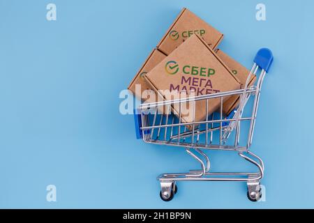 SberMegaMarket ist ein russischer Marktplatz im Besitz der Sberbank. Modifiziertes Foto von Paket mit SberMegaMarket Logo im Warenkorb auf blauem Hintergrund Stockfoto