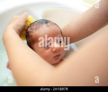 Erstes Bad des neugeborenen Jungen.die Mutter wäscht das Baby mit natürlichem Schwamm. Stockfoto