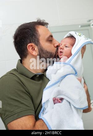 Erstes Bad des neugeborenen Jungen. Das Baby liegt im Bademantel in den Armen seines Vaters. Stockfoto