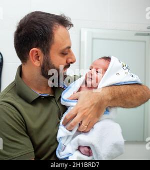 Erstes Bad des neugeborenen Jungen. Das Baby liegt im Bademantel in den Armen seines Vaters. Stockfoto