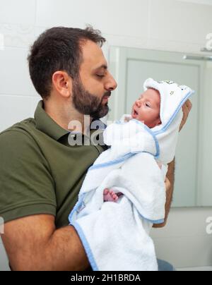 Erstes Bad des neugeborenen Jungen. Das Baby liegt im Bademantel in den Armen seines Vaters. Stockfoto