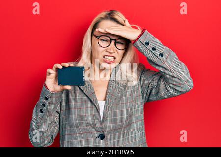 Schöne kaukasische blonde Geschäftsfrau hält ssd-Speicher gestresst und frustriert mit Hand auf Kopf, überrascht und wütend Gesicht Stockfoto