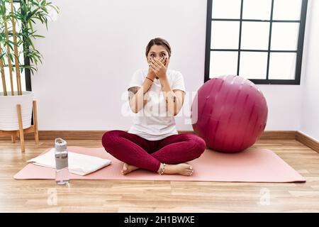 Junge hispanische Frau, die im Sportzentrum trainiert, schockierte den Mund fälschlicherweise mit Händen zu bedecken. Stockfoto