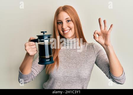 Junge irische Frau mit französischer Kaffeemaschine tut ok Zeichen mit den Fingern, lächelnd freundlich gestikulieren ausgezeichnete Symbol Stockfoto