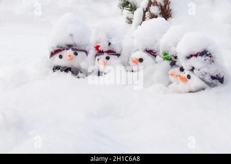 Fünf kleine niedliche Schneemänner, die mit einem frischen Schneefall bedeckt sind und Hüte und Schals und Karottennasen tragen. Winterschnee Spaß und Homour Landschaft Stockfoto