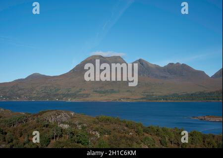 Blick über den Wald und Loch Torridon zum Beinn Alligin Berg in den schottischen Highlands. Sonniger Tag mit Blau. Freie Sicht auf die Riteline, Hörner von Alligin Stockfoto