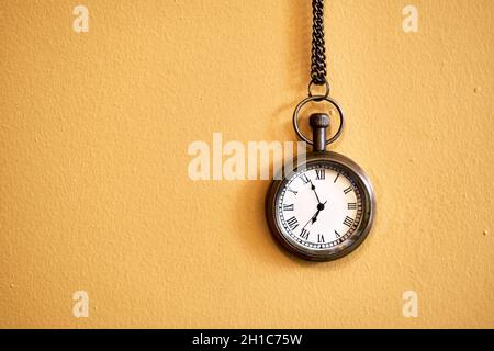 Vintage-Taschenuhr, die an einer gelben Wand mit Platz für Kopien hängt. Ablauf Countdown oder Zeitkonzept. Stockfoto