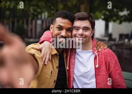 Junger Mann mit Down-Syndrom und sein Mentor-Freund, der im Freien Selfie nad Lookig vor der Kamera nimmt Stockfoto
