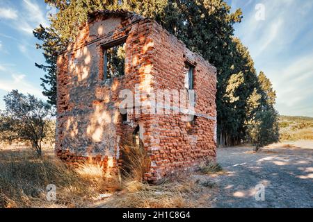 Ruinen eines verlassenen zweistöckigen Backsteinhauses, das sich außerhalb eines ländlichen Wiesenfeldes befindet. Stockfoto
