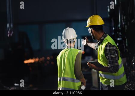 Rückansicht von Industrieinspektoren, die in Innenräumen in der Metallwerkstatt eine allgemeine Überprüfung durchführen. Stockfoto