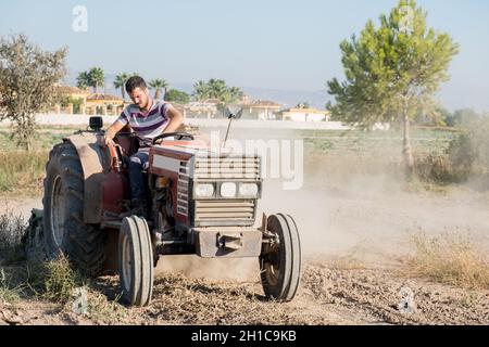 Der junge Bauer pflügt das Feld in seinem Traktor, umgeben von einer Staubwolke Stockfoto