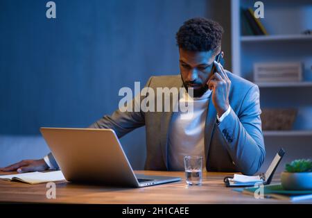 Junger afroamerikanischer Geschäftsmann, der nachts im Büro telefoniert. Stockfoto