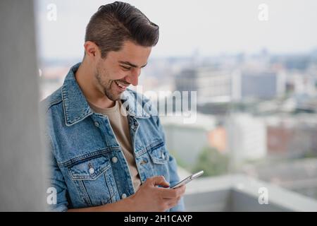 Porträt eines jungen kaukasischen Mannes mit Smartphone auf dem Balkon. Stockfoto